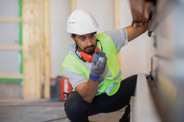 Miğferli ve ceketli işçi ahşap bir salonda çalışıyor.