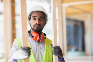 Miğferli ve ceketli işçi ahşap bir salonda çalışıyor.