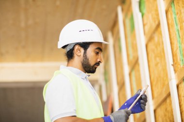 Miğferli ve ceketli işçi ahşap bir salonda çalışıyor.