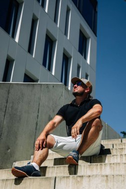 Şapkalı ve güneş gözlüklü adam modern binaya karşı.