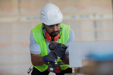 Kask ve güvenlik ceketli işçi ahşap salonda çalışıyor.