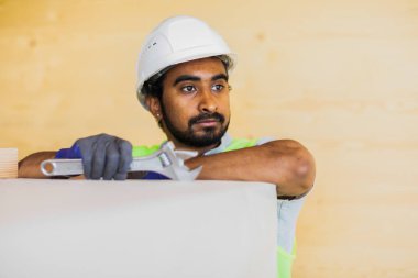 Miğferli ve ceketli işçi ahşap bir salonda çalışıyor.