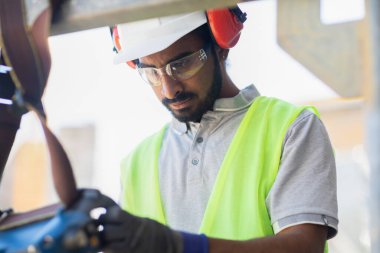 Miğferli ve ceketli işçi ahşap bir salonda çalışıyor.