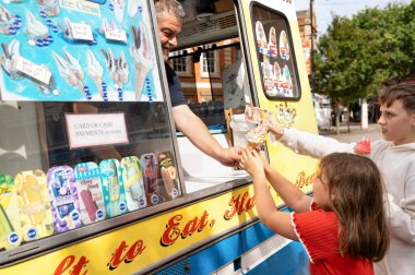 Çocuklar güneşli bir günde dondurma kamyonundan dondurma alıyorlar..