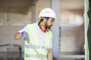 Miğferli ve ceketli işçi ahşap bir salonda çalışıyor.