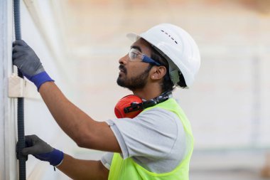 Miğferli ve ceketli işçi ahşap bir salonda çalışıyor.