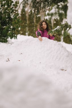 Pembe ceketli çocuk açık havada karlı bir tepeciğin üzerinde oynuyor.