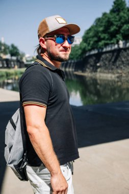 Güneş gözlüklü adam şehir güneşinde kanal kenarında duruyor.