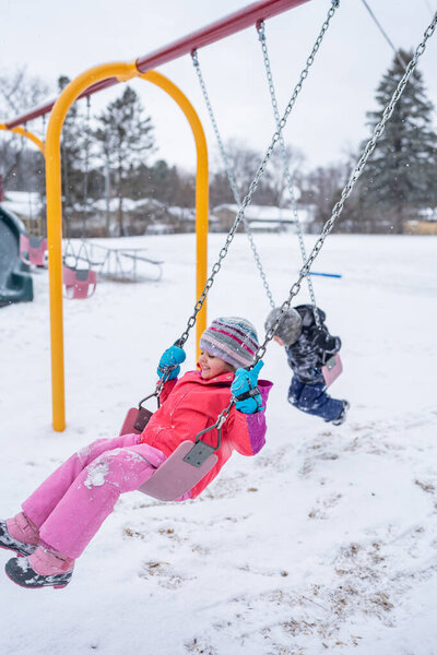 Children swinging on snowy day.
