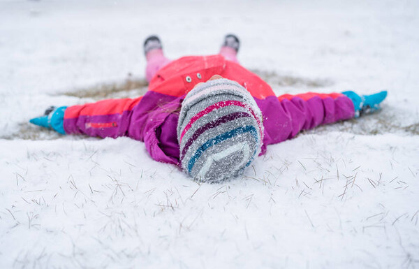 Child making snow angel on a snowy day.