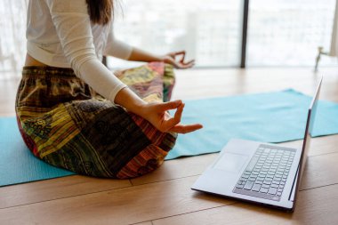 Renkli pantolonlu kadın yerde oturmuş meditasyon yapıyor.
