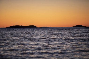 Ufuktaki adaların üzerinde gün batımı ve önlerinde okyanus.