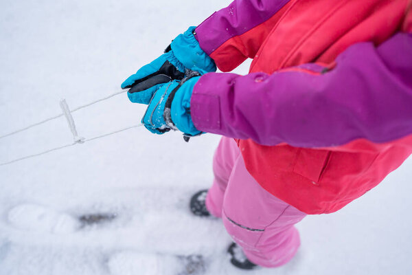 Young girl close up of mittens pulling sled.