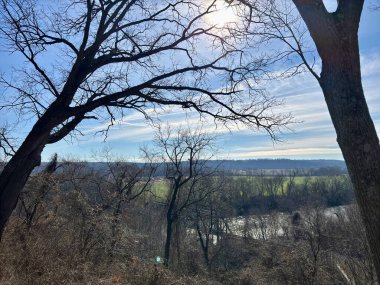 Çıplak ağaçlarla, yuvarlanan tarlalarla ve bir nehirle manzaralı.
