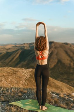 A woman practices yoga on a mat atop a mountain