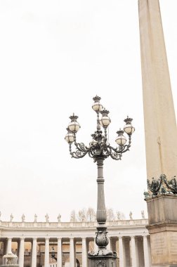 Ornate lamp post and tall obelisk in a grand plaza with colonnades