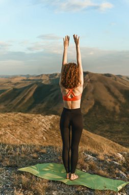 A woman practices yoga on a mat atop a mountain