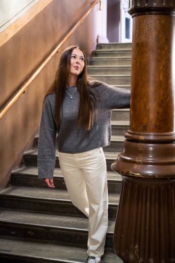 Klasik klasikleşmiş iç dekorasyonla merdivenlerde poz veren zarif genç bir kadın.