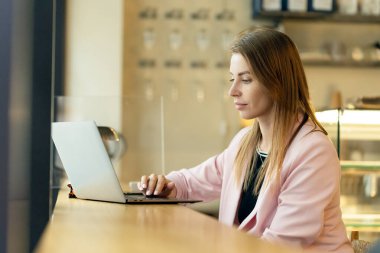 Modern şehir kafesinde dizüstü bilgisayarla çalışan genç kadın portresi.