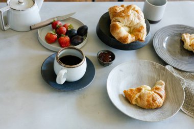 Breakfast setting with coffee, croissants, strawberries, and jam