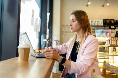 Bir kafede dizüstü bilgisayarda çalışan genç bir kadın.