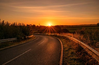 Curved countryside road with the rising sun on the horizon.
