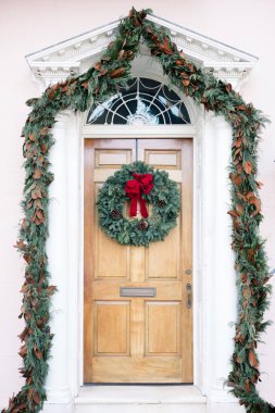 Festive doorway with a wreath, garland, and holiday greenery.