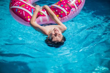 Çocuk şişme bir donut tutarken sırt üstü yüzüyor.