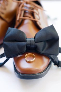 Brown leather shoe with black bow tie and gold wedding ring on top.