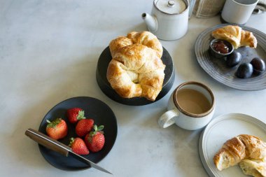 Breakfast table with croissants, coffee, strawberries, and plums