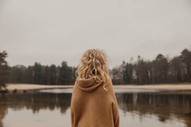 Suyu yansıtan ağaçlarla sakin bir gölün yanında yürüyen bir çocuk..