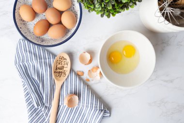 Overhead view of cracked eggs, shells, and brown eggs in bowl