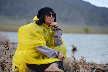 Göl kenarındaki sarı yağmurluklu kadın.