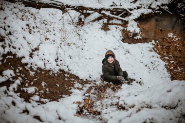 Çocuk kış mevsiminde karlı orman zemininde oynuyor