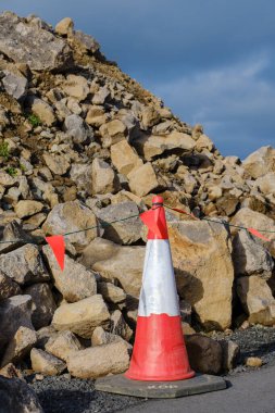 A cone with red and white stripes on it next to a pile of rocks