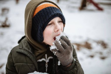 Genç çocuk karlı kış gününde dışarıda kartopu yiyor.