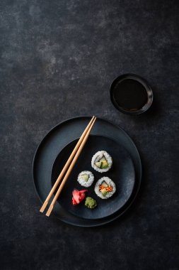 Overhead view plate of sushi rolls and chopsticks on black background.