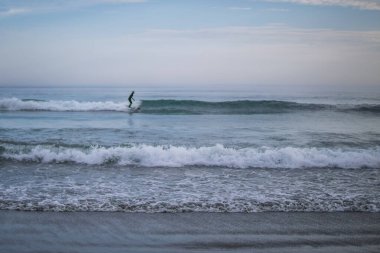 Kumsalda kumla ve mavi gökyüzüyle okyanusta sörf yapan sörfçü.