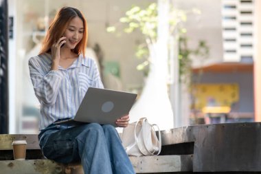 Kadın bankta oturuyor ve cep telefonuyla konuşuyor.