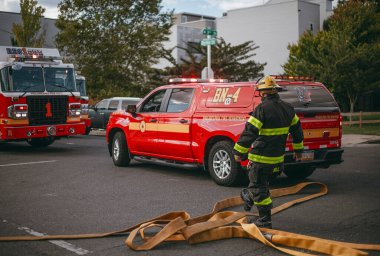 İtfaiyeci hortumu itfaiye aracının arka planına dayar.