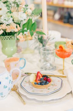Elegant table with floral centerpiece, fruit tart, and pink cocktail.