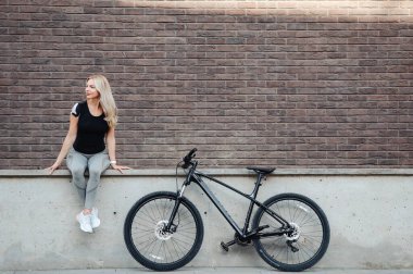 Bisikletle tuğla duvarda dinlenen kadın