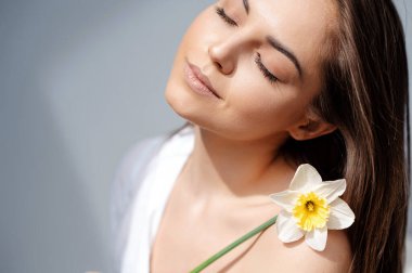 Gri stüdyo arka planında poz veren nergis çiçeği tutan şefkatli bayan.