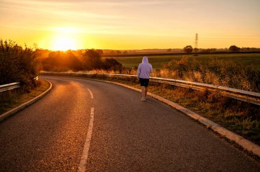 Gün doğumunda sakin bir kırsal yolda yürüyen bir adam..