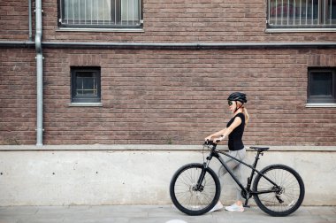 Kasklı kadın bisikletçi. Sokakta siyah duruyor.