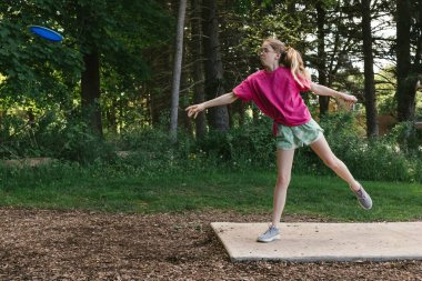 Kız disk golf oynarken ormanda golf sopası kutusundan fırlatıyor.