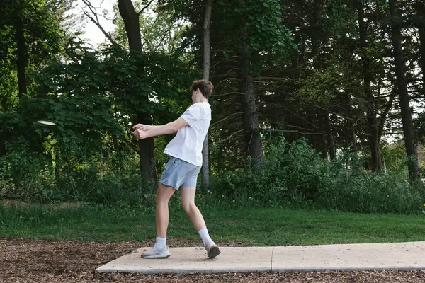 Genç, ormanda disk golfü oynarken diski kutusundan fırlatıyor.