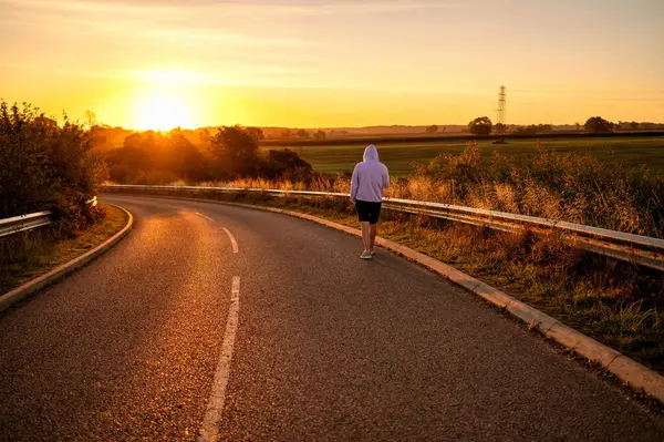 Gün doğumunda sakin bir kırsal yolda yürüyen bir adam..