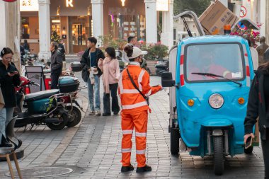 HAINAN, ÇİN, 20 ARALIK 2024: Qilou Eski Caddesi 'ndeki çöpleri temizlemek için üç tekerlekli arabanın yanında duran kadın hademe