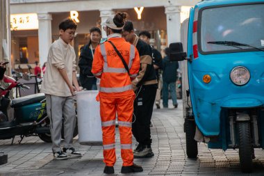 HAINAN, ÇİN, 20 ARALIK 2024: Qilou Eski Caddesi 'ndeki çöpleri temizlemek için üç tekerlekli arabanın yanında duran kadın hademe